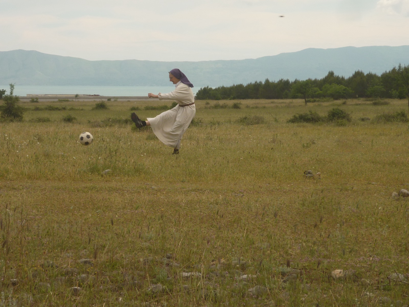 Schwester Michaela kickt einen Fussball auf einer weiten Wiese am See.
